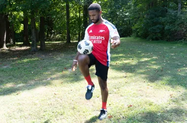 A man in a soccer jersey juggling a soccer ball on his knee