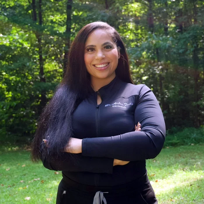 Dr. Amber Jones standing with arms crossed, outside and surrounded by trees.