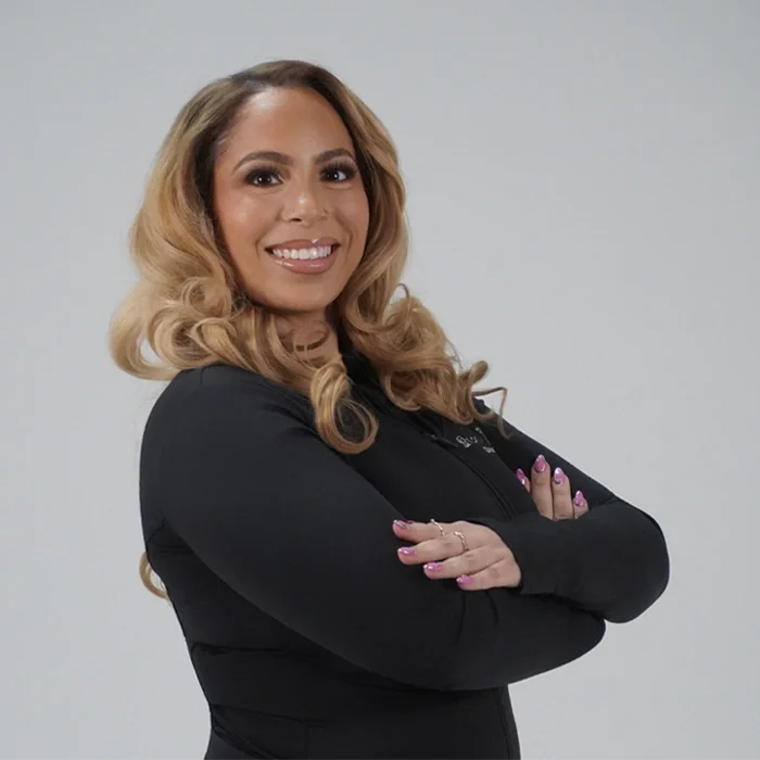 Dr. Amber Jones standing with arms crossed against a gray studio background.
